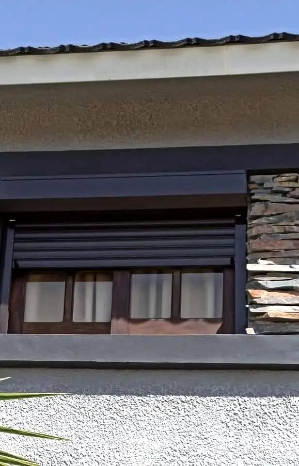 Cortina de enrollar de aluminio color madera en una casa con fachada de piedra
