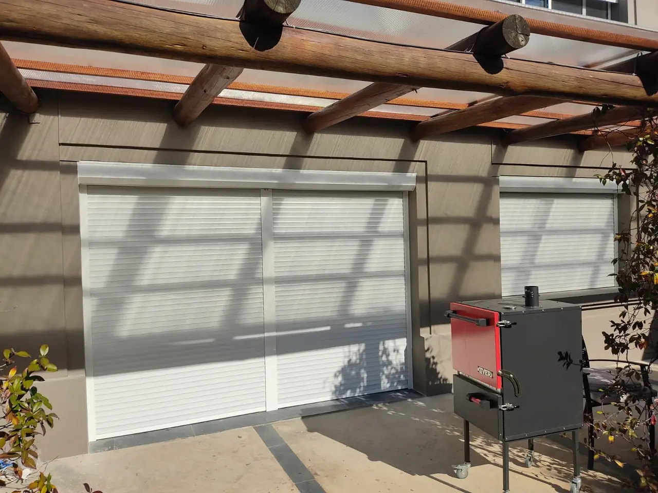 Cortinas de enrollar blancas en un ventanal bajo una pérgola de madera