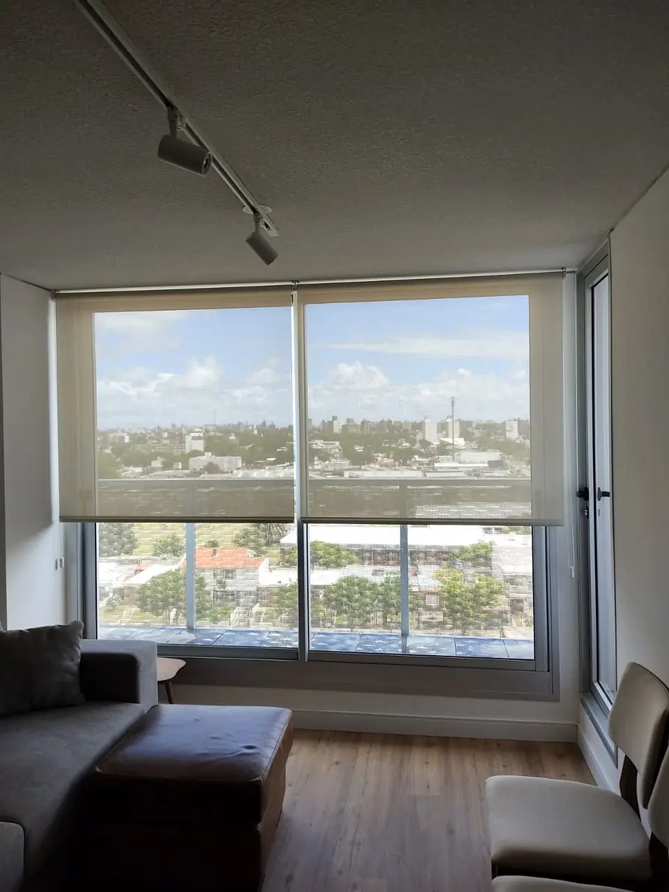 Cortina roller screen en un ventanal de apartamento con vista a la ciudad