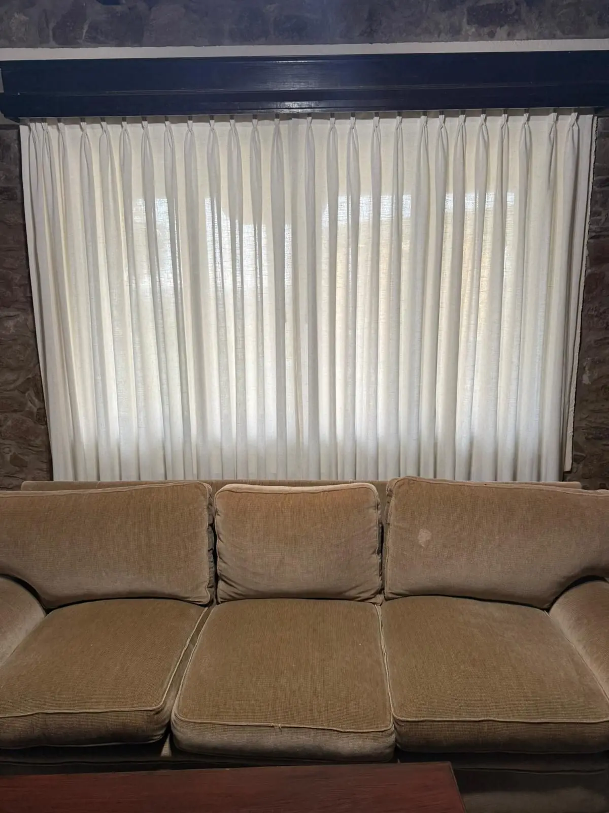 Cortinas tradicionales de tela clara en el ventanal de un living, detrás de un sillón