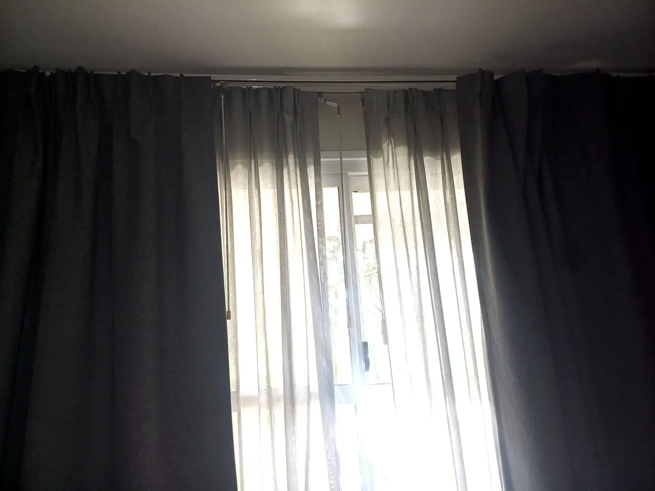 Cortinas tradicionales de doble capa en una ventana: blackout gris a los lados y tela liviana al centro